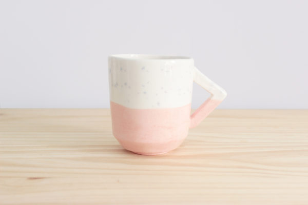 Taza realizada a mano con diseño de asa rectangular en loza blanca en tonos rosas y azules